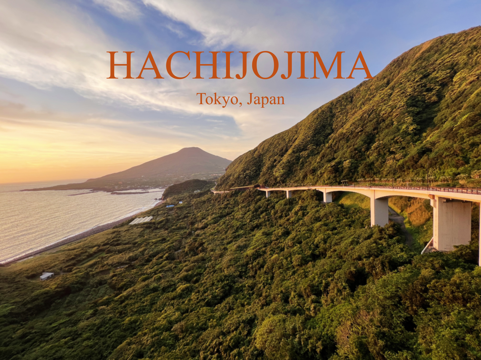 Panoramic sunset view from Osaka Tunnel Observatory in Hachijojima, Tokyo, featuring a coastal bridge and the silhouette of Hachijo-kojima island.